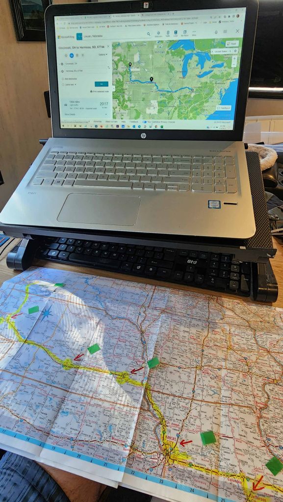 A laptop and paper map with various marks and a highlighted route.