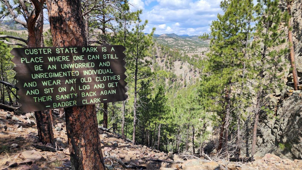 A sign with a quote from Badger Clark against a scenic view of the Black Hills of South Dakota in Custer State Park.
