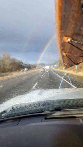 View out of truck windshield with double rainbow in the distance through the rain.