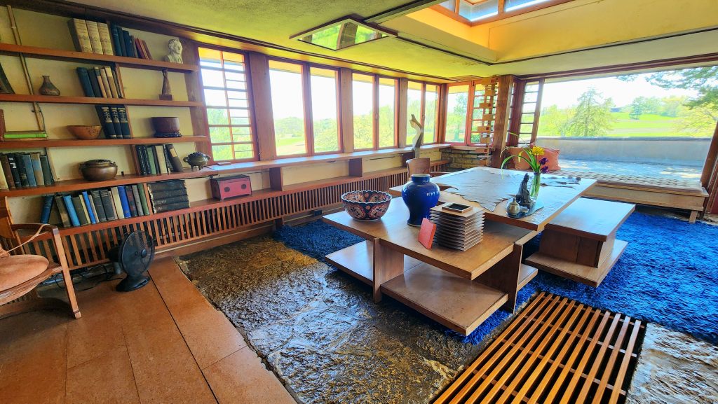 Living area at Taliesen, Frank Lloyd Wright's home showcasing furniture and views of the valley through numerous windows.