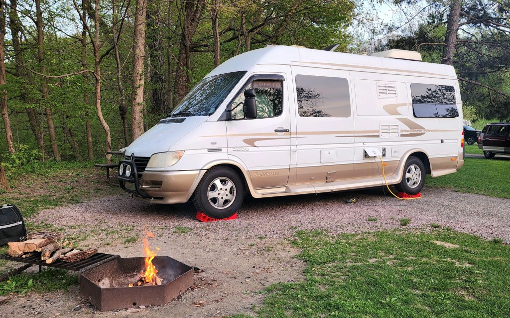 Campfire with firewood and Pleasure Way camper van at a campsite.