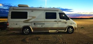 Pleasure Way camper van parked in gravel at Dakota Dunes casino against a backdrop of a sunset.