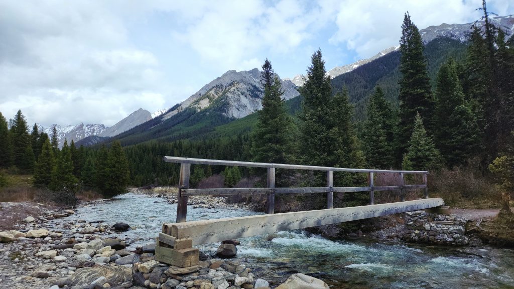 wood narrow walking bridge over river full of rocks in Banff National Park