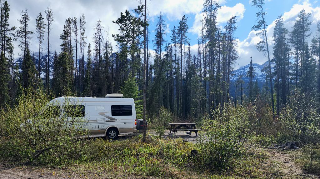 van parked among trees at a campsite surrounded by mountains