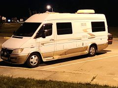 RV van parked at a rest area for the night with a dark sky and dim lighting.