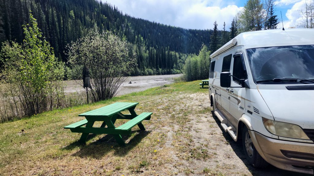 van parked alongside a river next to a picnic table